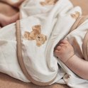 Un bébé allongé dans une cape de bain avec un imprimé d'ours brun. Une petite main de bébé est visible.