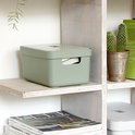 Groene opbergbox met een deksel, waarop een patroon is gedrukt, staat op een plank met tijdschriften.