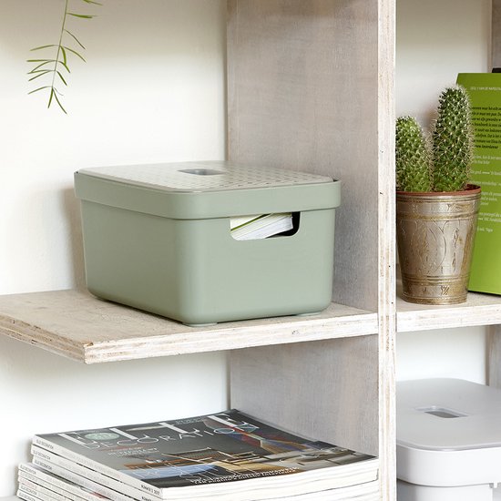 Groene opbergbox met een deksel, waarop een patroon is gedrukt, staat op een plank met tijdschriften.