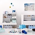 Lego opbergmeubel met blauwe en grijze blokken, babybed en speelgoed in een kinderkamer.