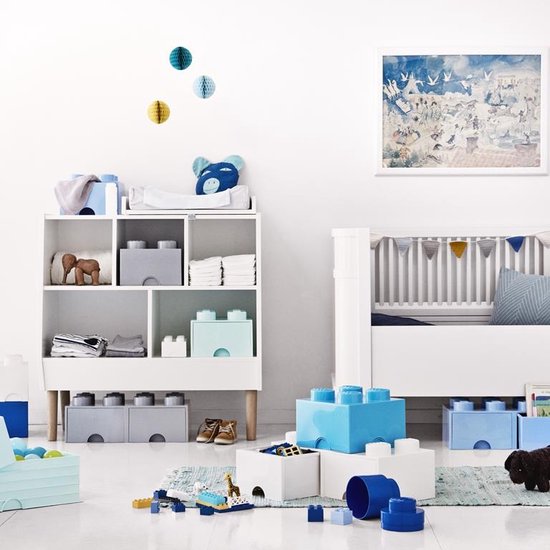Lego opbergmeubel met blauwe en grijze blokken, babybed en speelgoed in een kinderkamer.