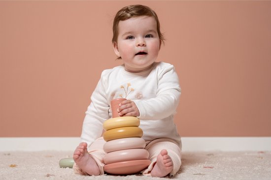 Baby met stapelringenset. De baby houdt een groene ring voor de mond, de roze stapelringenset ligt naast de baby.