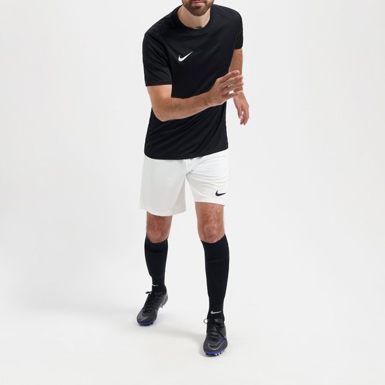 Homme en tenue de sport, comprenant un t-shirt Nike noir, un short blanc et des chaussettes noires, debout avec les genoux pliés.
