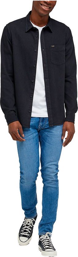 Man in een donkerblauw overhemd met lange mouwen, een wit T-shirt en een spijkerbroek.