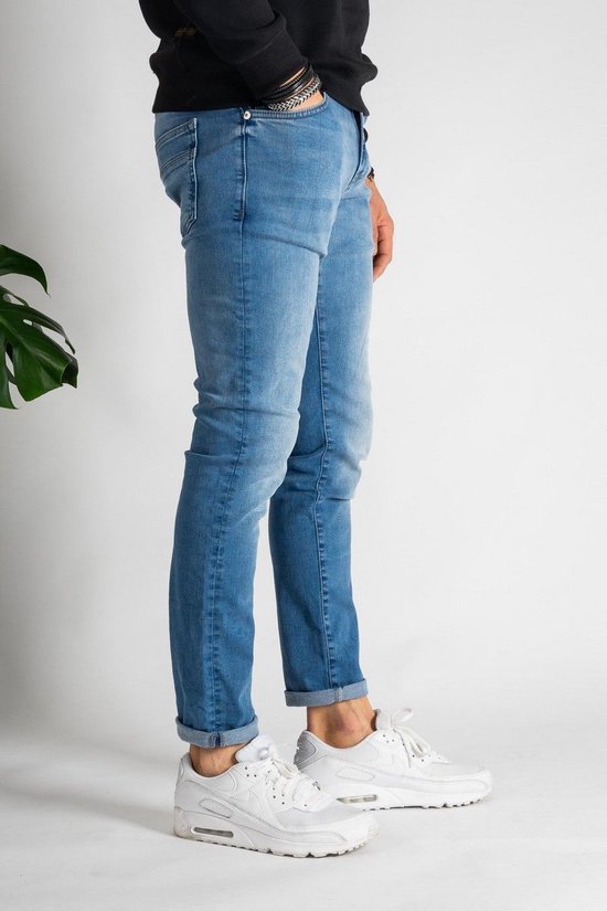 Man in een lichtblauwe spijkerbroek met opgerolde zoom en witte sneakers, gezien vanaf de zijkant, met detail van de zakken en het Cars Jeans logo.