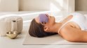 Femme allongée avec un masque pour les yeux violet sur les yeux.