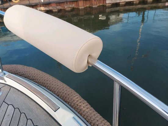Crème relingkussen op een bootdek, bevestigd aan een metalen reling, met water op de achtergrond.