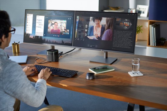 Een persoon werkt aan een bureau met twee monitoren, een laptop en een zwarte muis.