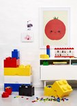 Gestapelde rode, gele, witte en blauwe Lego-opbergdozen met een zwarte doos op de grond.