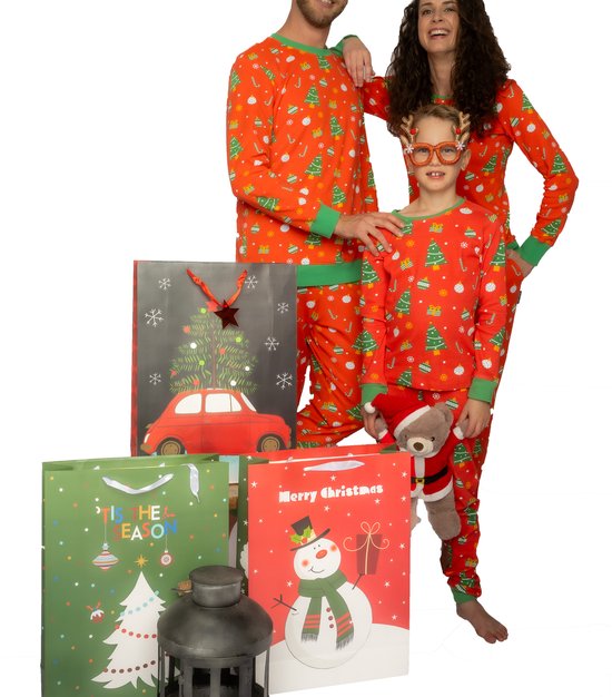 Familie in oranje kerstpyjama's met groene boorden, met kerstbomen, snoepstokken en sneeuwvlokken. Een jongen draagt een rendierbril en een knuffelbeer.