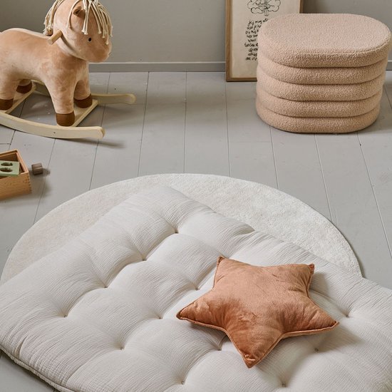 Crème, capitonne speelkleed met een oranje sterrenkussen, op een rond wit kleed.