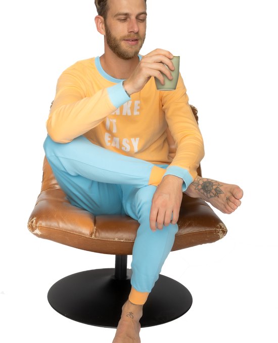 Man in oranje pyjamashirt 'TAKE IT EASY' en lichtblauwe broek zit op stoel met koffie.