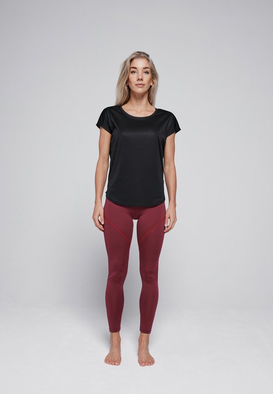 Model met blonde haren, draagt een zwarte sporttop met korte mouwen en een rode legging. Ze staat frontal.