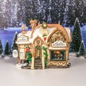 Verlicht Lemax gebouw met 'Devaney's Bakery' en 'Ye Olde Tea Shoppe' in sneeuw.