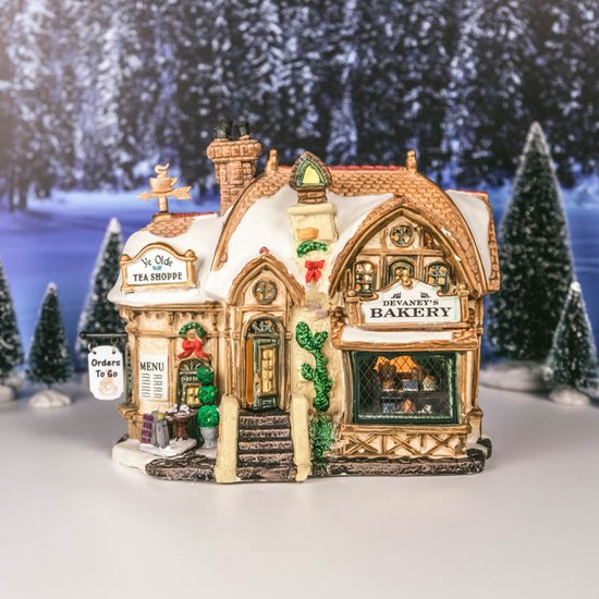 Verlicht Lemax gebouw met 'Devaney's Bakery' en 'Ye Olde Tea Shoppe' in sneeuw.