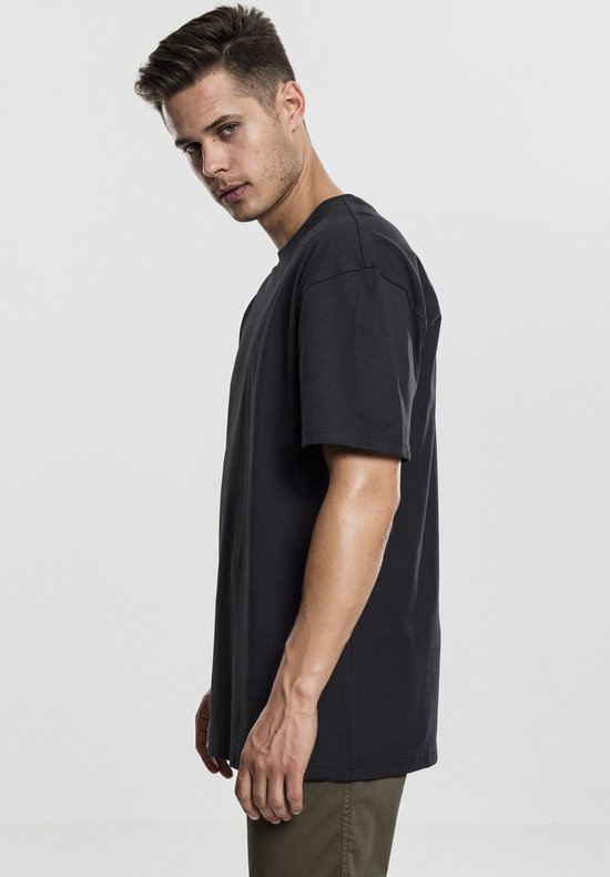 Man, zijaanzicht, draagt een donkergrijs oversized T-shirt met korte mouwen.