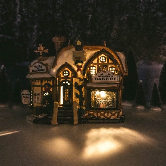 Verlicht Lemax 'Devaney's Bakery' gebouw in besneeuwd landschap.