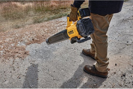 Man met gele DeWalt bladblazer, blaast vuil van bestrating.