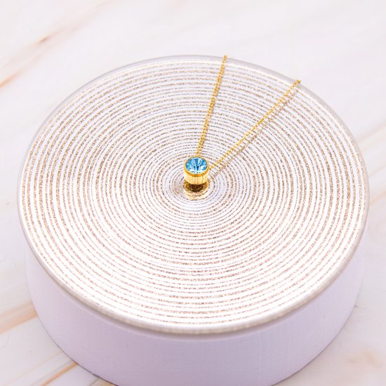 Gouden ketting met blauwe zirkonia op display met gouden cirkels.