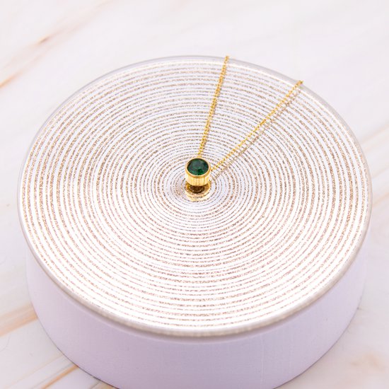 Gouden ketting met smaragdgroene hanger op een zilveren display met spiraalpatroon.