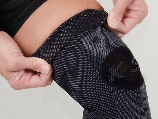 Handen die de rand van een zwarte compressie kniebrace met antislip stippen laten zien.