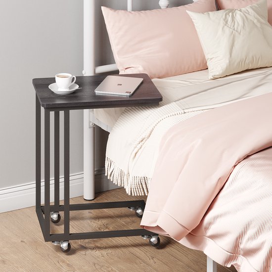 Zwart bijzettafeltje op wieltjes, naast een bed, met een kopje koffie en een tablet.