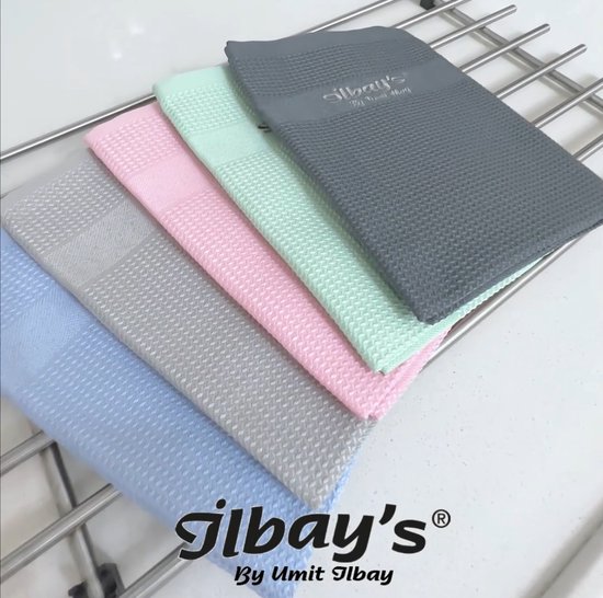 Cinq lingettes microfibre Jilbay's aux couleurs pastel claires et gris foncé, sur un étendoir métallique.