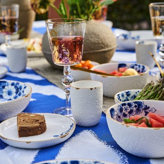 Gedekte tafel met blauw-witte gestreepte tafelkleed, glazen met roze drank, en servies met blauwe bloemen.