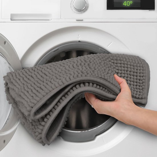 Hand legt een grijze badmat met bobbelstructuur in een wasmachine.