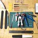 Table de loisirs créatifs avec une maquette Gundam, pinces, couteau, limes, chiffon de polissage et séparateur.