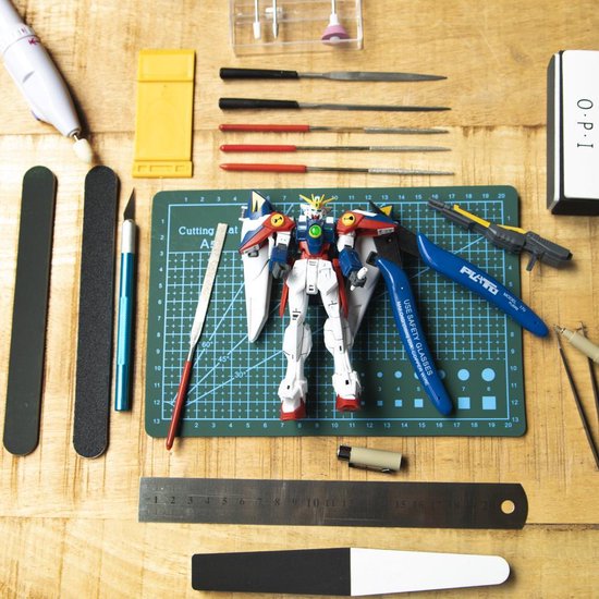 Table de loisirs créatifs avec une maquette Gundam, pinces, couteau, limes, chiffon de polissage et séparateur.