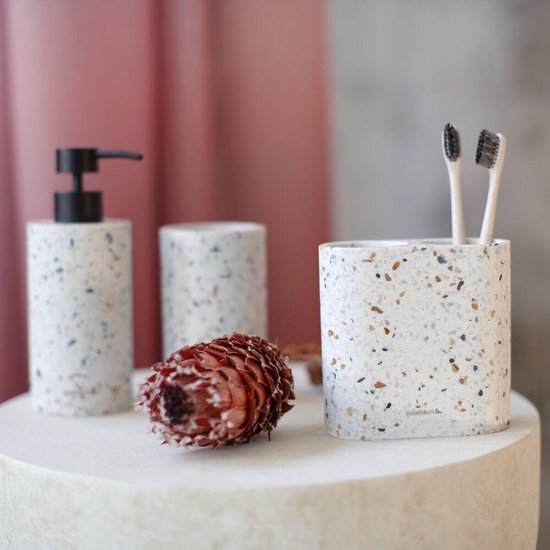 Zeepdispenser en tandenborstelhouder met terrazzo-look op een wit plateau, met een decoratieve bloem.