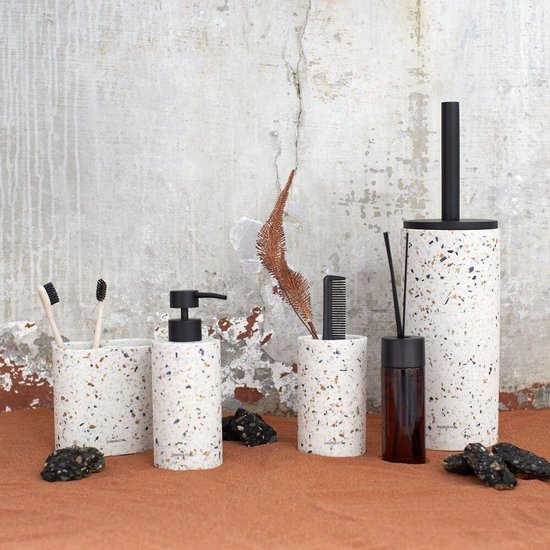 Set badkameraccessoires met terrazzo-look, waaronder tandenborstelhouders, een zeepdispenser en een houder voor toiletborstel, geplaatst op een zandkleurige ondergrond.