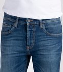Detail van de voorkant van een donkerblauwe spijkerbroek met oranje stiksels.