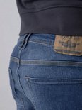 Close-up achterkant van een spijkerbroek in blauw denim met een bruin label van 'Petrol Industries'.
