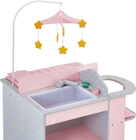 Grijze commode met witte stippen, roze matras. Badje met douchekop en een mobiel met gele sterren erboven.