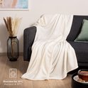 Een witte fleece deken ligt losjes over een stoel. Wasbaar op 30°C.