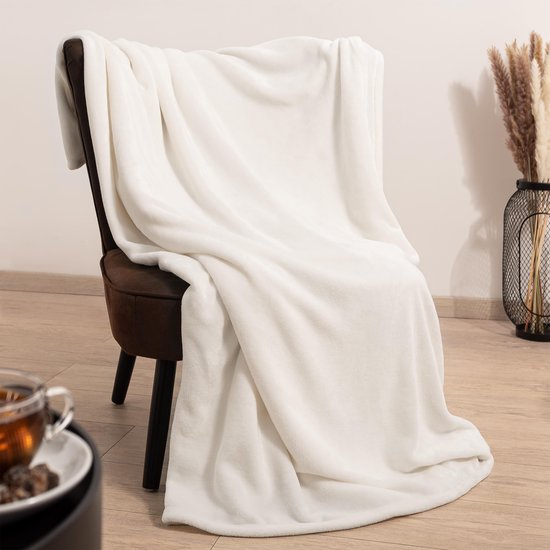 Een witte fleecdeken hangt over een bruine stoel, met een kopje thee ernaast.
