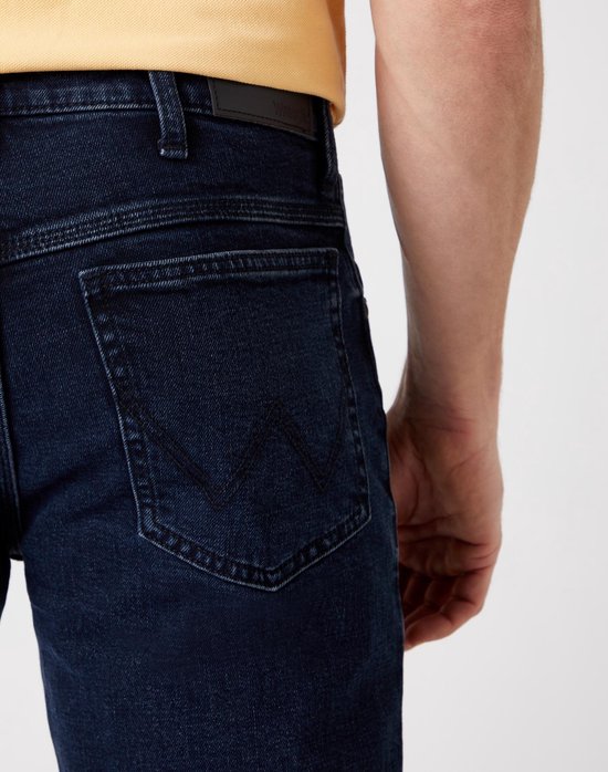 Close-up van de achterzakken van een donkerblauwe spijkerbroek met Wrangler logo.