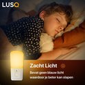 Witte LUSQ nachtlamp in de vorm van een stekker, geeft zacht geel licht. Slapen met een kind op de achtergrond.