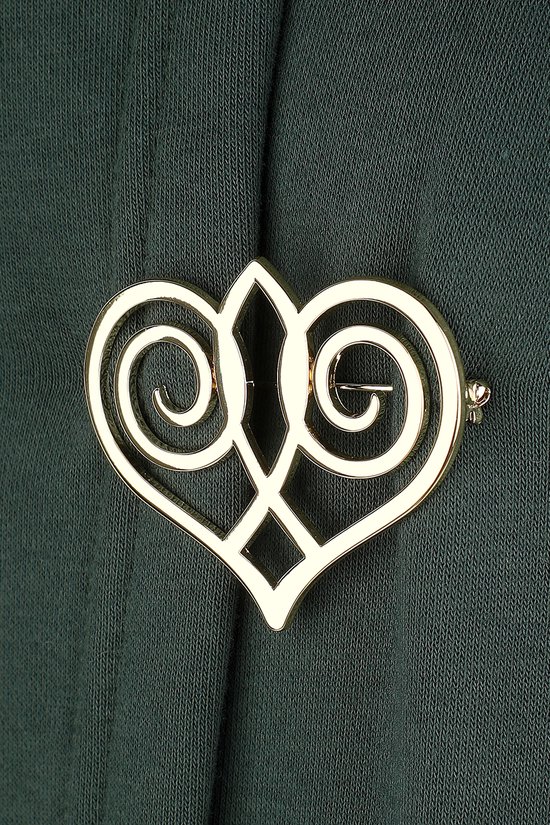 Gouden hartvormige broche met keltische knopen, bevestigd op een donkergroene stof.