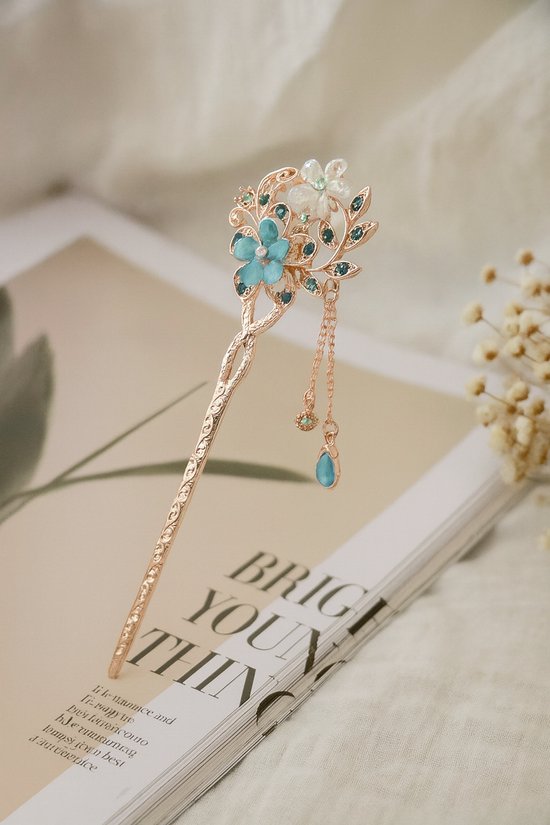 Épingle à cheveux dorée avec des fleurs bleues et des pierres bleues sur un magazine.