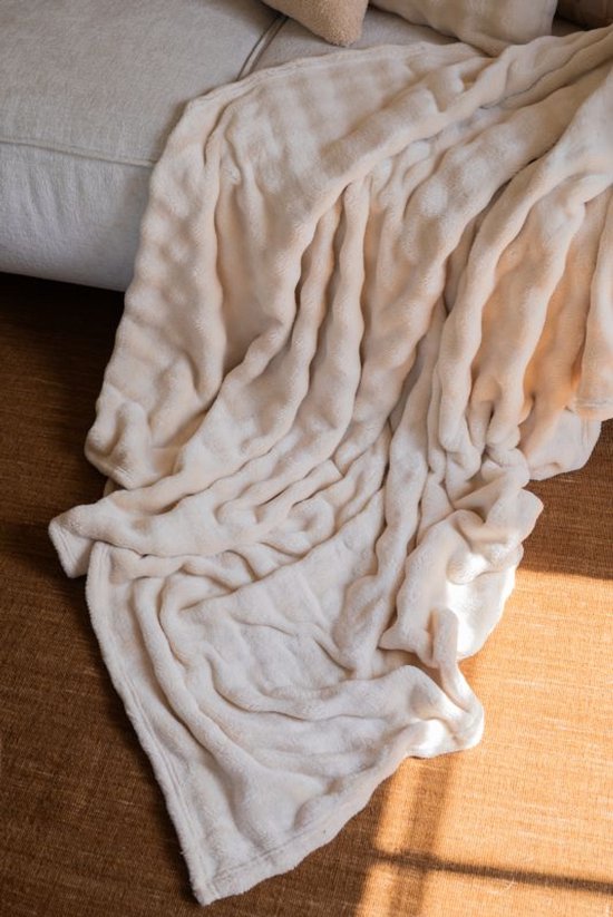 Een crème plaid met subtiele textuur, uitgestald op een bruine vloer.