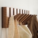 Detail van een houten kapstok met 10 beweegbare haken, met een beige sjaal en jas.