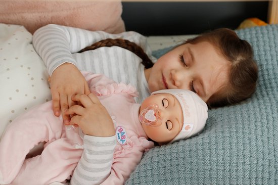 Meisje slaapt met baby pop in roze pyjama in bed. Baby Annabell.