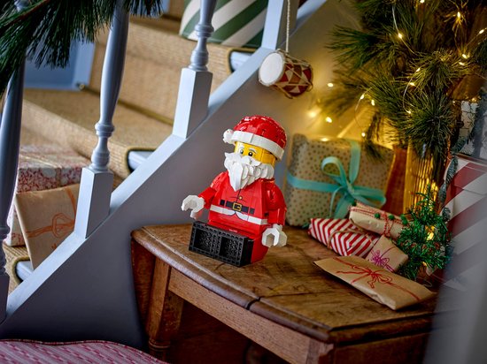 LEGO opgeschaalde Kerstman minifiguur in rood pak, zittend op een houten meubel.