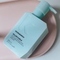 Lichtblauwe pompflacon van KEVIN.MURPHY Killer.Curls op een roze schaal, met tekst.