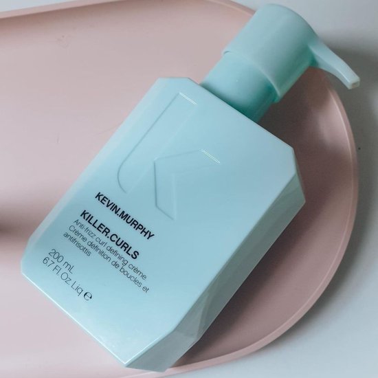 Lichtblauwe pompflacon van KEVIN.MURPHY Killer.Curls op een roze schaal, met tekst.