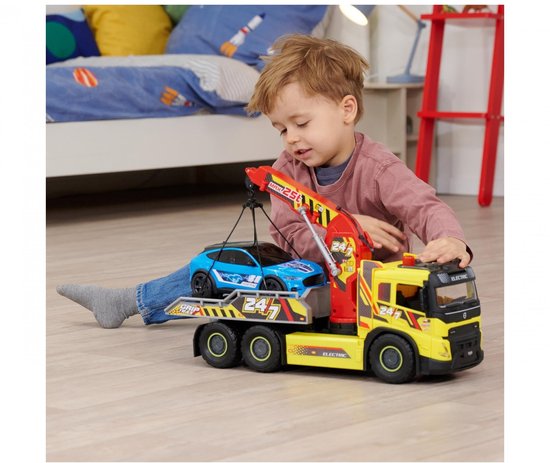 Jongen speelt met gele takelwagen met rode kraan die een blauwe Ford Mustang optilt.