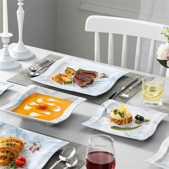 Gedekte tafel met marmerblauwe borden. Een bord met steak, groenten en aardappelen, een bord met pastasaus, een bord met gebak en een glas water.
